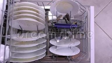男人`手在洗碗机里用脏盘子推篮子。